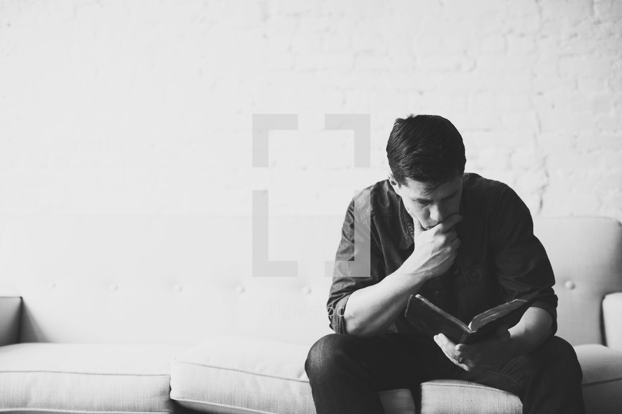 Man sitting on a sofa reading the Bible.
