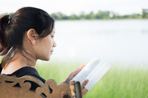 a woman reading a Bible sitting on a park bench 