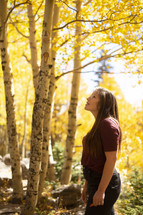 a woman looking up at fall trees 
