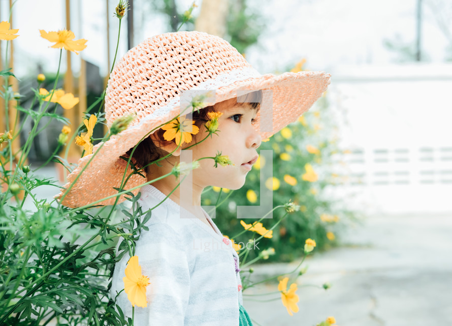 a little girl in a sunhat standing next to flowers 