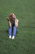 Teen girl sitting in green grass, looking to heaven, asking "why?"