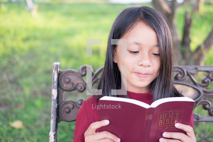 a girl reading a Bible sitting on a park bench 