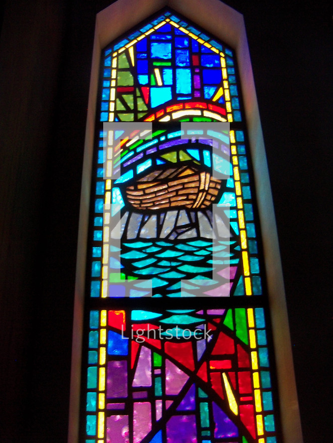 A full length stained glass window depicting the ark built by Noah resting on dry land surrounded by receding waters and an over arching rainbow showing God's promise to man to never destroy the world by flooding ever again. 