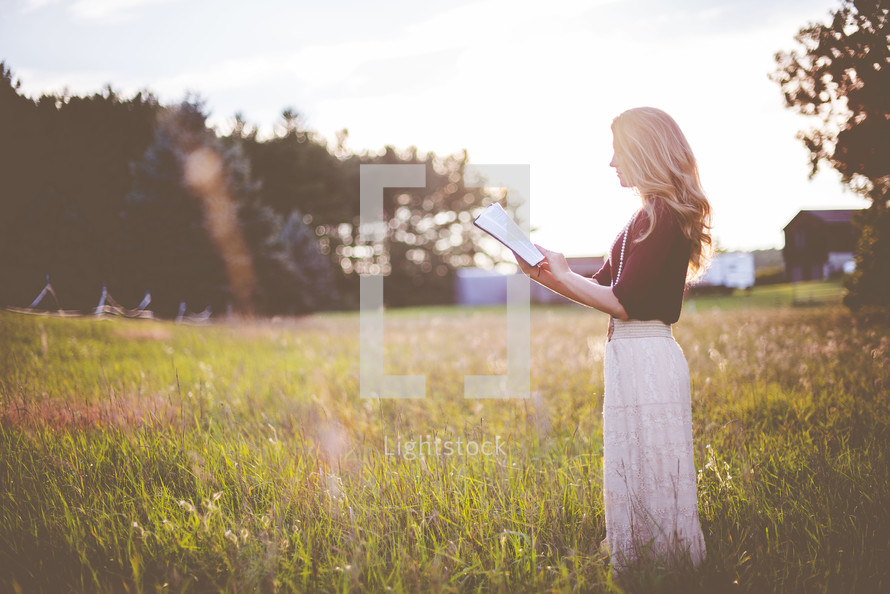 a woman standing in a field reading a Bible 