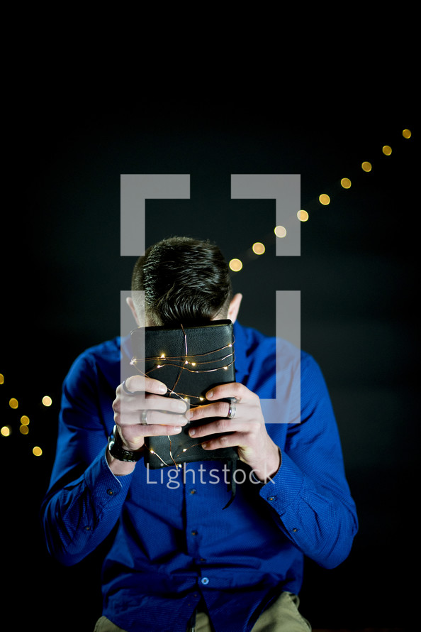 a man holding a Bible wrapped in fairy lights 