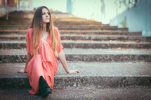 young woman sitting on outdoors stairs wearing red dress.