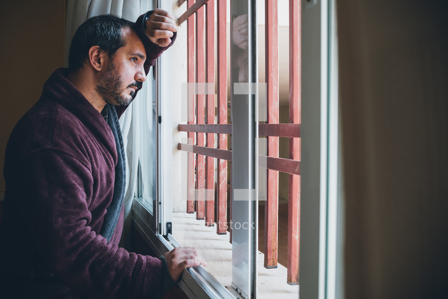 man looking out a window longingly 