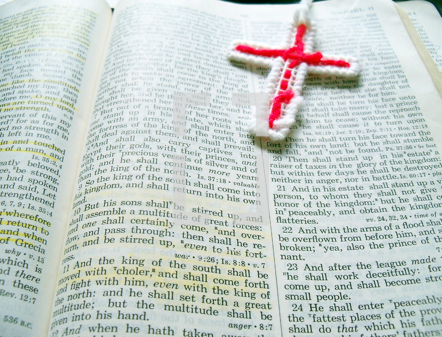 A well read bible is open with a red cross needle point bookmark and highlighted bible verses during quiet time bible study and reading God's word. 