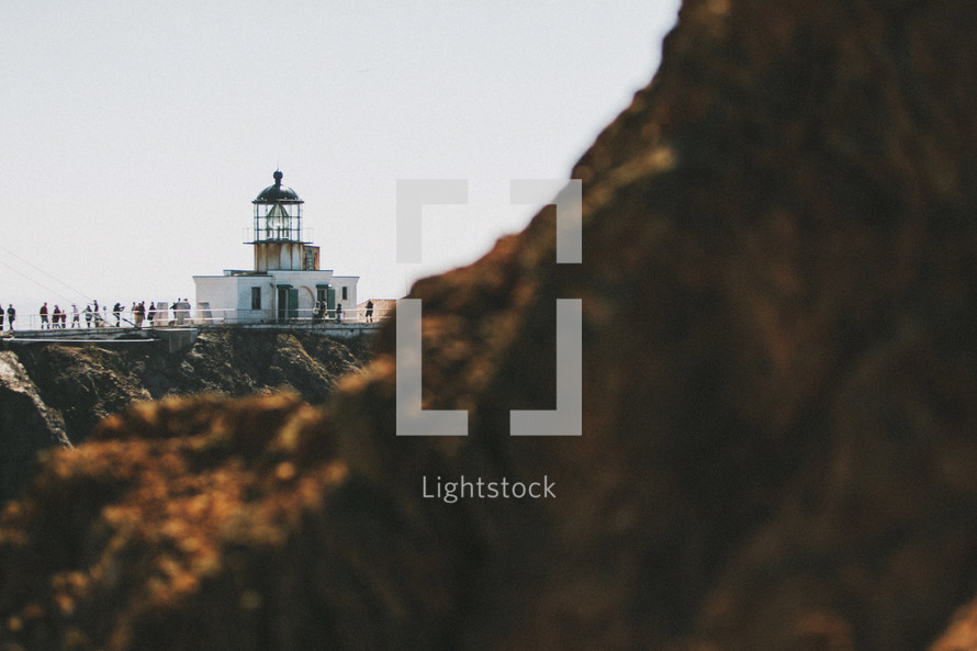 A lighthouse beyond a rocky cliff.