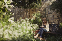 Woman reading bible on bench in garden,