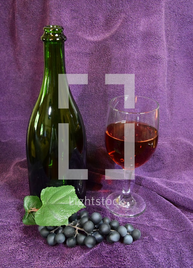 Wine bottle and glass and a bunch of grapes, with a purple cloth background 
