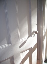An old white painted door knob on a white door bathed in morning sunlight.  