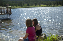 girls sitting on a lake shore 