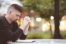 man praying with head bowed reading a Bible 