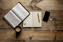opened Bible, journal, coffee cup, pen, cellphone, and earbuds 
