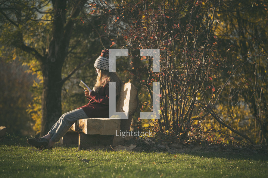 a teen girl sitting on a bench outdoors reading a Bible 