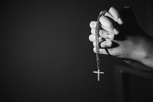 Black and white image of a woman holding a rosary and praying. 