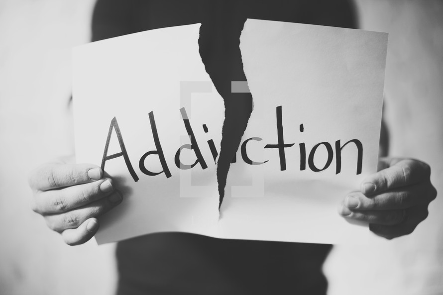 tearing apart a piece of paper with the word addiction on it 