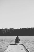 Woman sitting on a dock by a lake.