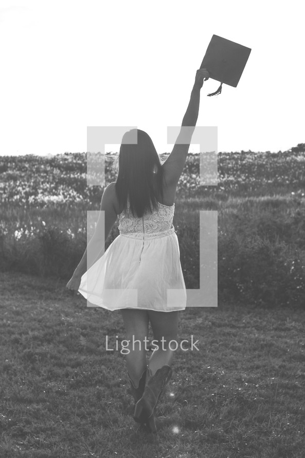 a young woman standing in cowboy boots holding a graduation cap 