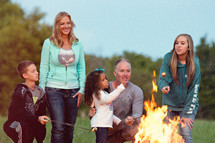 a family standing by a camp fire roasting marshmallows 