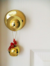 A brass Jingle Bell with a red bow adorns a brass door knob against a white background adding color, warmth and the feelings of the holidays, snow and Christmas warmth and cheer to an otherwise ordinary door entrance allowing the bell to jingle every time the door is opened to help announce visitors and guests coming in for the holidays. 