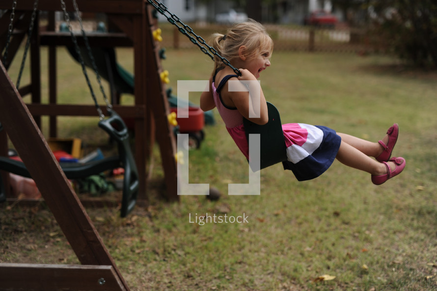 a little girl on a backyard swing set 