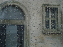 Rain drops on a window overlooking church windows.