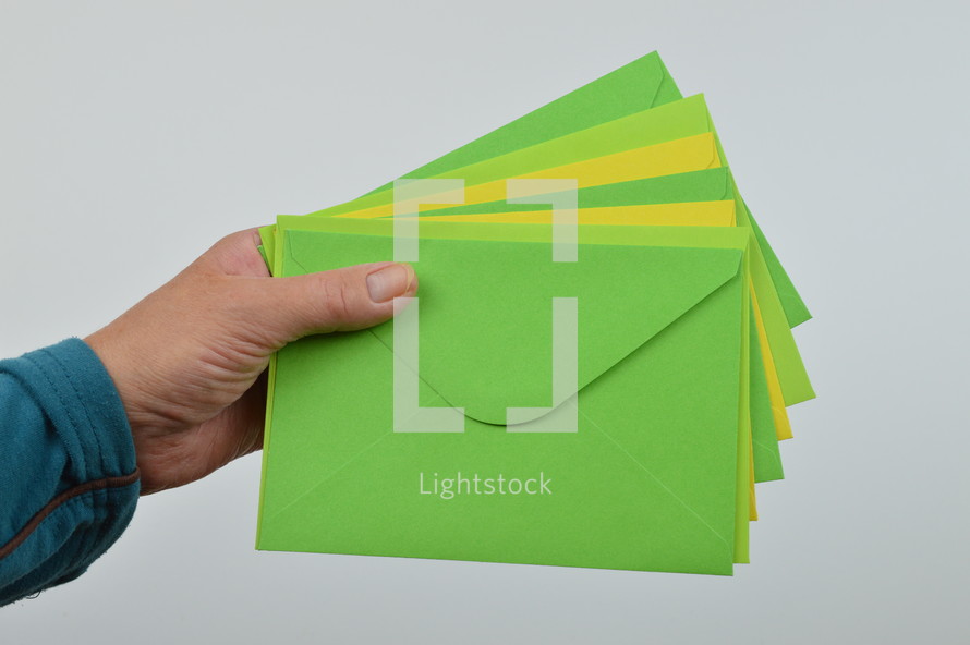 holding envelopes - person holding a pile of yellow and green envelopes in hand in front of white background 