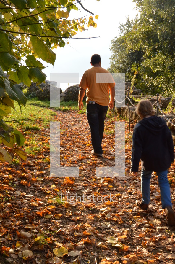 father and daughter walking on a path covered in fall leaves 