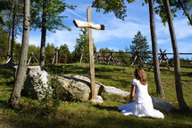 woman kneeling in prayer in front of a wood cross outdoors 