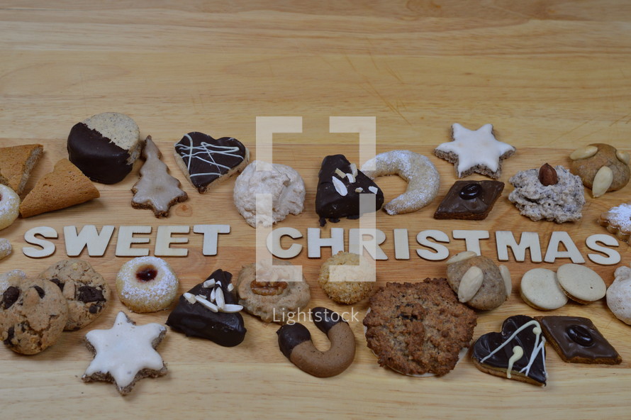 different kinds of Christmas cookies on a breadboard around the words: SWEET CHRISTMAS