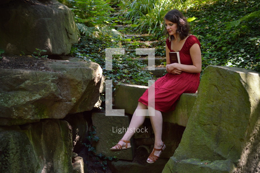 woman sitting in a forest holding a Bible 