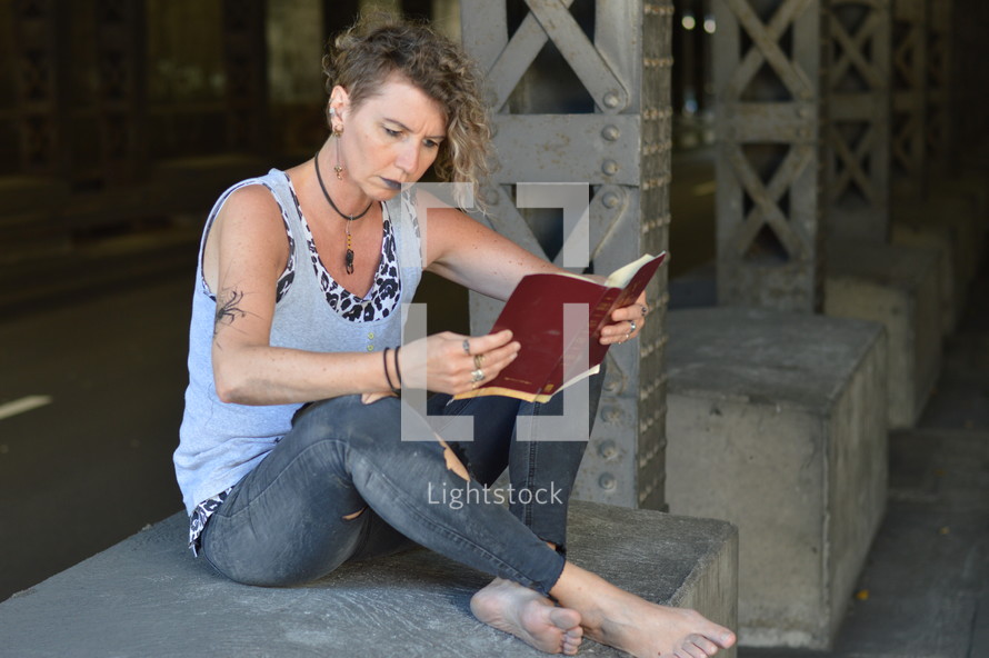 homeless woman reading a Bible under an overpass