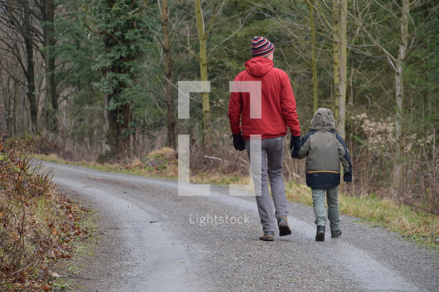 a man and a child walking down a road in the forest