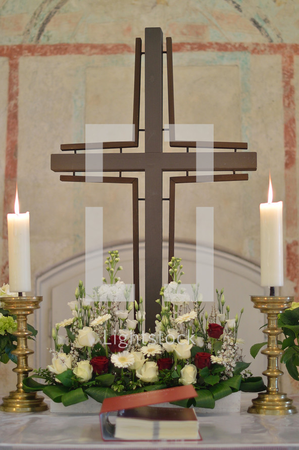 Cross, candle sticks and a flower arrangement on an altar. 