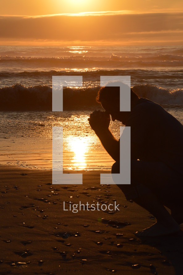 man praying at the beach in front of a sunset
