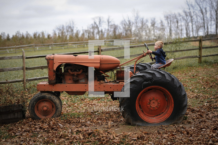 a boy child sitting on a tractor on a farm 