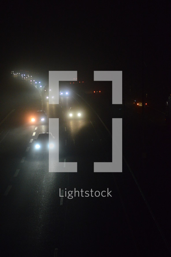 View from a bridge at a highway by night on a cold foggy winter night. 
