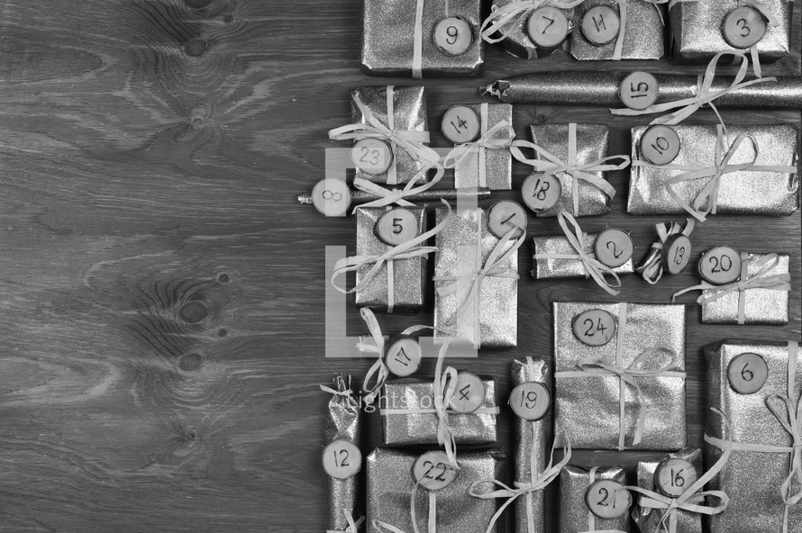 Border of advent calendar with twenty four silver presents on grey wood with negative space to the left