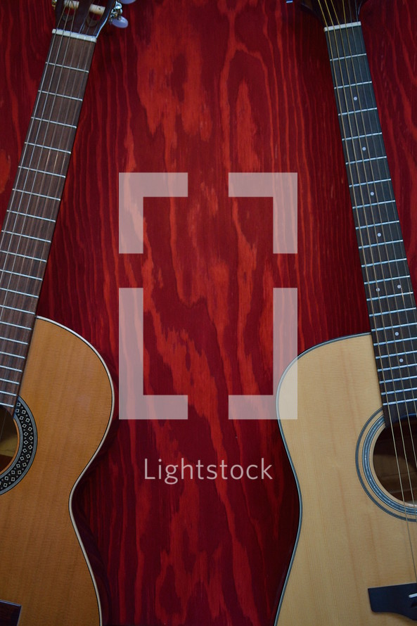 two acoustic guitars on red wooden background