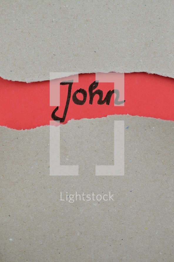 John - torn open kraft paper over light red paper with the name of the Gospel of John