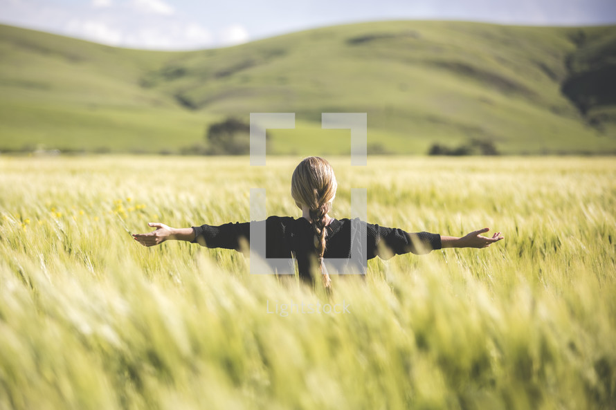 a woman standing in a field of wheat with outstretched arms 