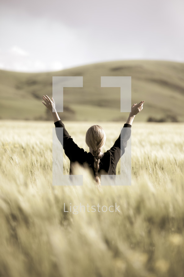 a woman with raised hands standing in a field of wheat 