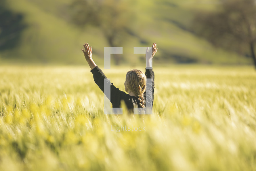 a woman standing in a field of wheat with raised arms 