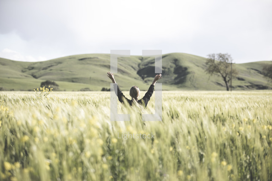 a woman with raised arms standing in a field of wheat 