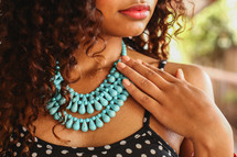 a young woman touching her teal beaded necklace 