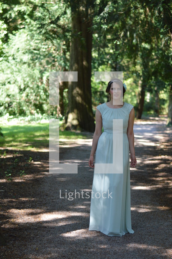 a woman in a vintage dress standing on a path in a forest 