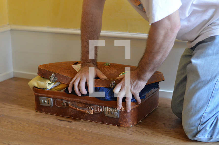 man trying to close his overstuffed suitcase