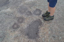 a boy standing next to spots on a rock surface 